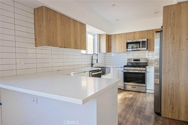 kitchen featuring sink, hardwood / wood-style flooring, appliances with stainless steel finishes, tasteful backsplash, and kitchen peninsula