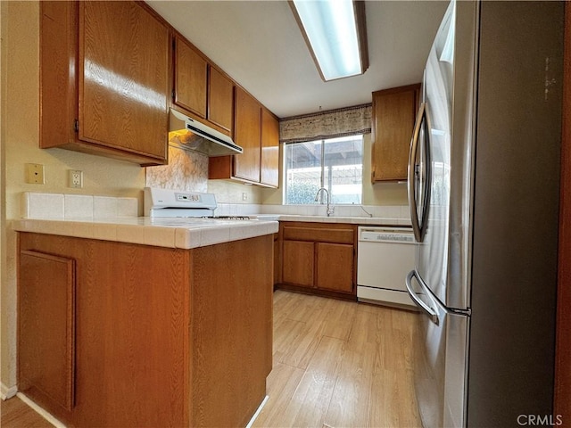 kitchen with stainless steel refrigerator, dishwasher, stove, tile counters, and light wood-type flooring