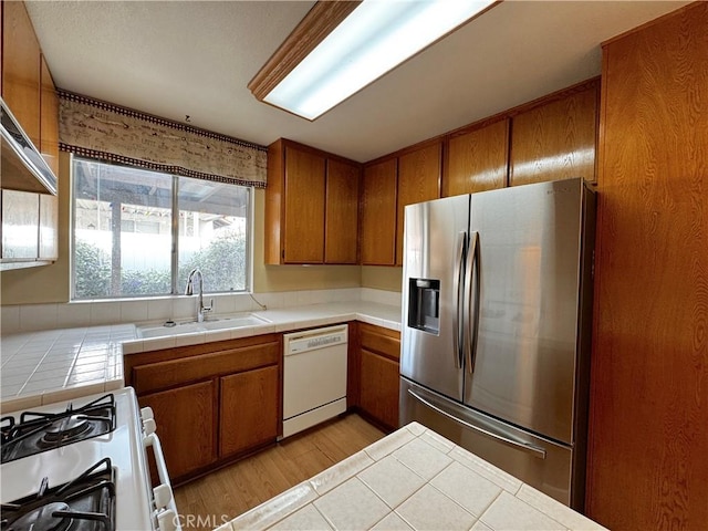 kitchen with sink, tile counters, white appliances, and light wood-type flooring