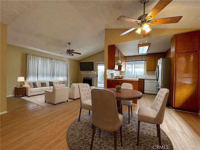 dining area with a tiled fireplace, lofted ceiling, ceiling fan, and light hardwood / wood-style flooring