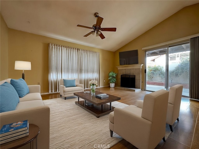 living room featuring a tile fireplace, vaulted ceiling, ceiling fan, and light hardwood / wood-style flooring