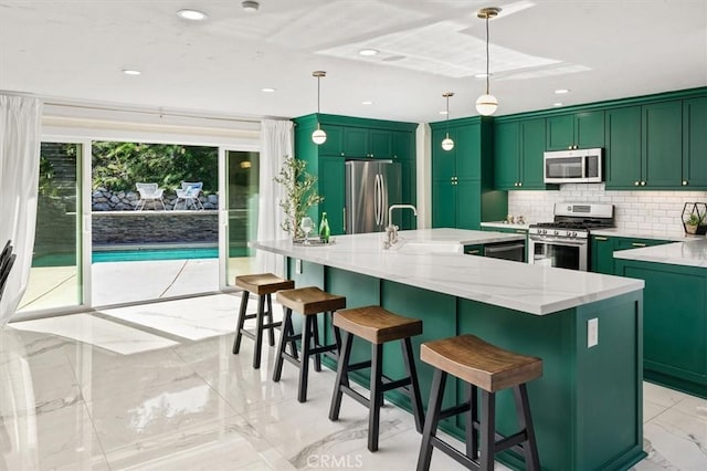 kitchen featuring appliances with stainless steel finishes, hanging light fixtures, light stone counters, and a center island with sink