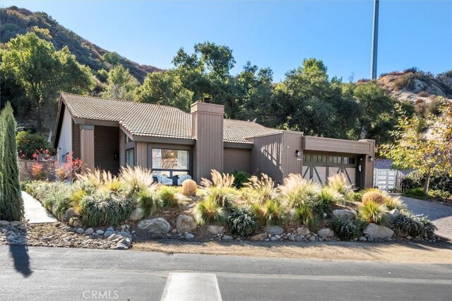 view of front of property with a chimney, an attached garage, a mountain view, driveway, and a tiled roof