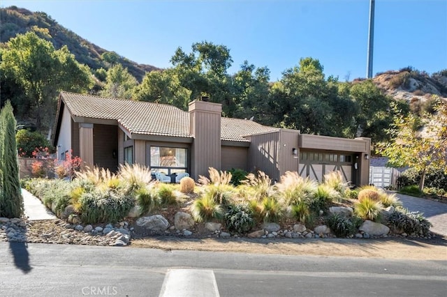 view of front of home with a garage, driveway, a tile roof, a chimney, and a mountain view