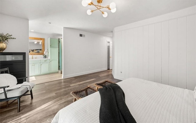 bedroom with baseboards, visible vents, ensuite bath, wood finished floors, and a chandelier