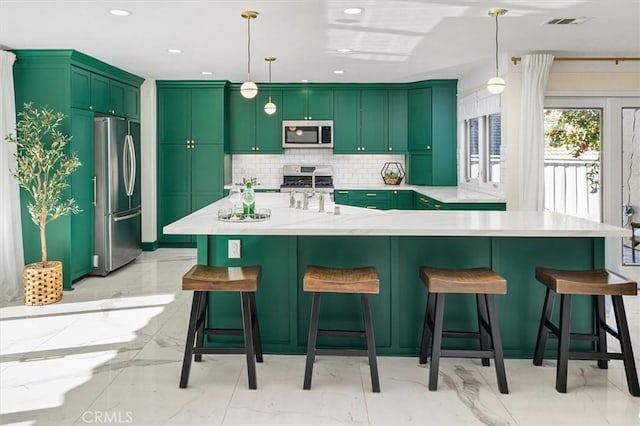 kitchen with a kitchen island with sink, stainless steel appliances, decorative light fixtures, and decorative backsplash