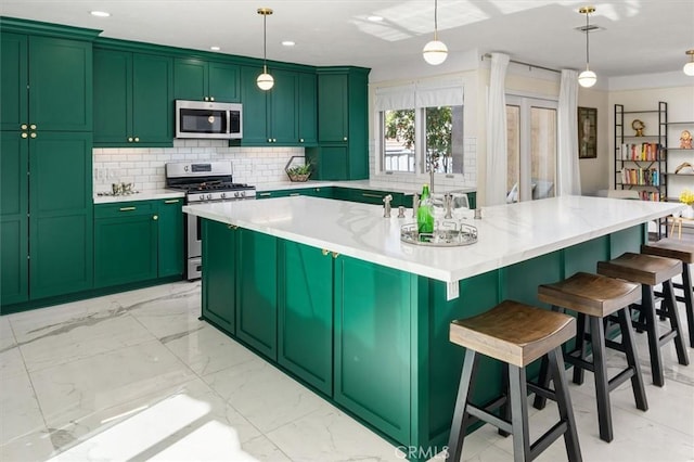 kitchen with appliances with stainless steel finishes, hanging light fixtures, backsplash, and a center island with sink