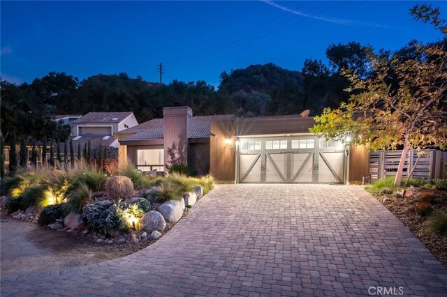 view of front of house with an attached garage, fence, a tiled roof, decorative driveway, and a chimney