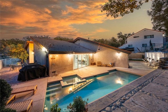 pool at dusk with a pool with connected hot tub, fence, grilling area, and a patio