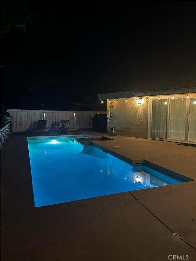 pool at twilight with a patio area and fence