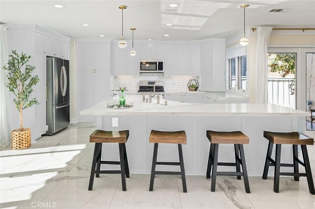 23726 La Salle Canyon Rd, Newhall, CA 91321 - kitchen featuring appliances with stainless steel finishes, light marble finish floors, white cabinetry, decorative backsplash, and a kitchen bar