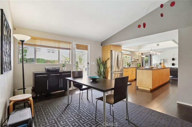 dining area with lofted ceiling, a notable chandelier, dark hardwood / wood-style floors, and a healthy amount of sunlight