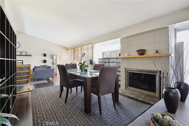 dining space featuring dark wood-type flooring, lofted ceiling, and a tile fireplace