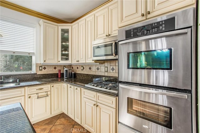 kitchen featuring dark tile patterned floors, appliances with stainless steel finishes, cream cabinetry, and dark stone counters