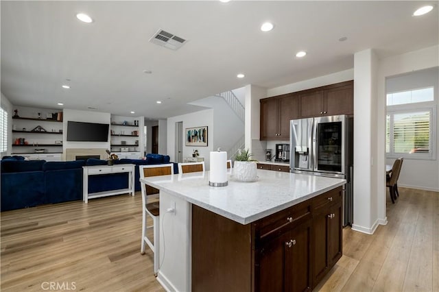 kitchen featuring a breakfast bar area, light stone counters, stainless steel fridge with ice dispenser, light hardwood / wood-style flooring, and a kitchen island