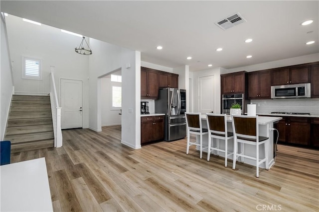 kitchen featuring a kitchen island, appliances with stainless steel finishes, a kitchen bar, dark brown cabinetry, and light hardwood / wood-style floors