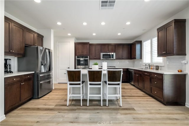 kitchen with appliances with stainless steel finishes, a center island, a breakfast bar, and dark brown cabinets