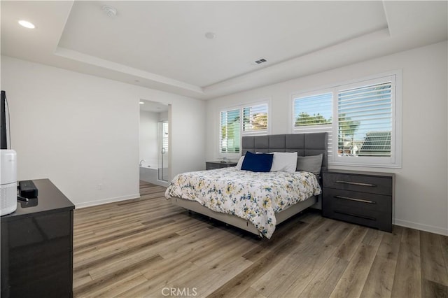 bedroom with wood-type flooring, connected bathroom, and a raised ceiling