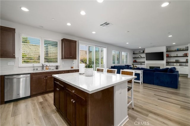 kitchen with sink, a breakfast bar, a kitchen island, stainless steel dishwasher, and light wood-type flooring