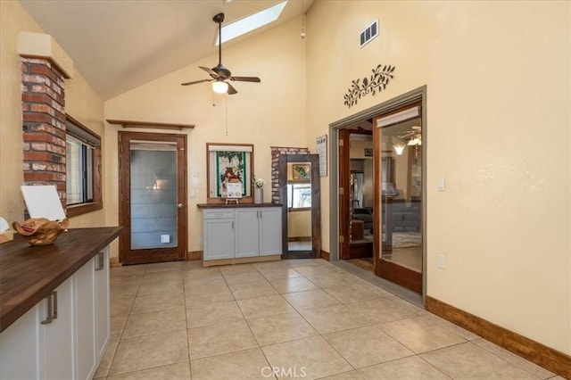 tiled foyer featuring a skylight, high vaulted ceiling, and ceiling fan