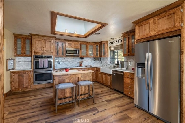 kitchen with sink, hardwood / wood-style flooring, appliances with stainless steel finishes, a kitchen island, and a kitchen bar