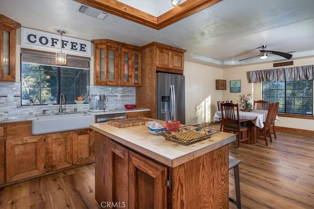 kitchen featuring pendant lighting, sink, a tray ceiling, stainless steel appliances, and light wood-type flooring