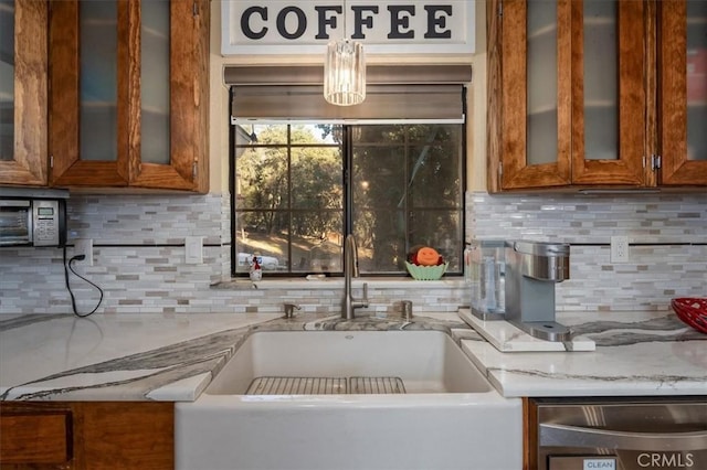 kitchen with hanging light fixtures, light stone countertops, sink, and backsplash