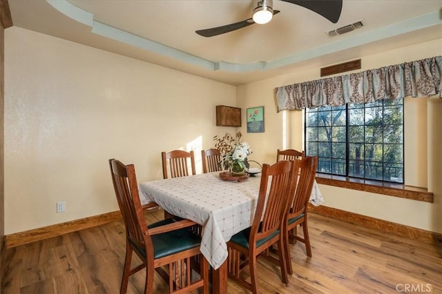 dining space with a tray ceiling, wood-type flooring, and ceiling fan