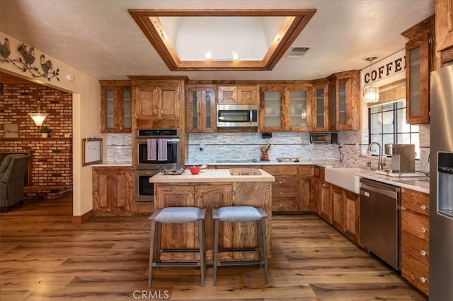 kitchen with appliances with stainless steel finishes, a breakfast bar area, decorative backsplash, hardwood / wood-style flooring, and a center island