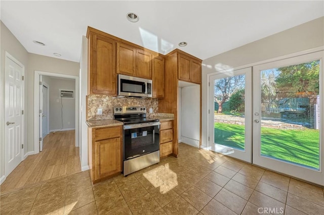 kitchen with light tile patterned floors, a wall unit AC, stainless steel appliances, decorative backsplash, and french doors