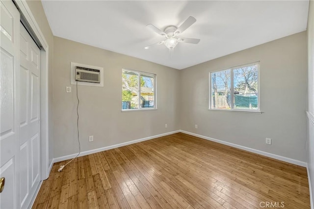 empty room featuring ceiling fan, light hardwood / wood-style flooring, a wall mounted AC, and plenty of natural light