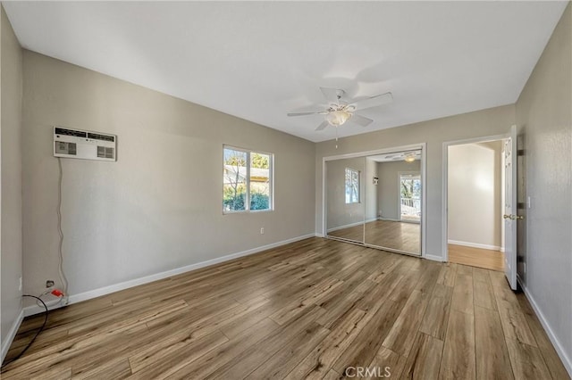 unfurnished bedroom with light wood-type flooring, an AC wall unit, a closet, ceiling fan, and multiple windows