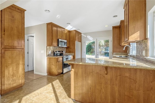 kitchen with appliances with stainless steel finishes, tasteful backsplash, light stone counters, light tile patterned flooring, and kitchen peninsula