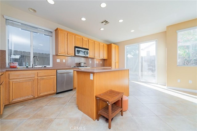 kitchen with a kitchen island, tasteful backsplash, appliances with stainless steel finishes, and light tile patterned floors