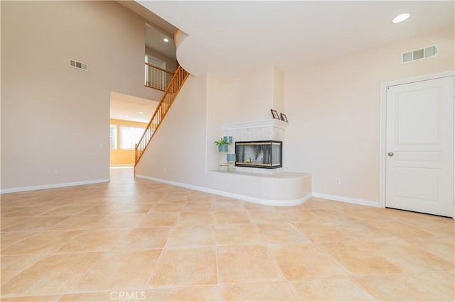 unfurnished living room featuring a high ceiling, a tile fireplace, and light tile patterned floors