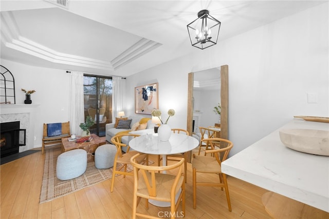 dining space with a high end fireplace, a tray ceiling, a chandelier, and light hardwood / wood-style floors