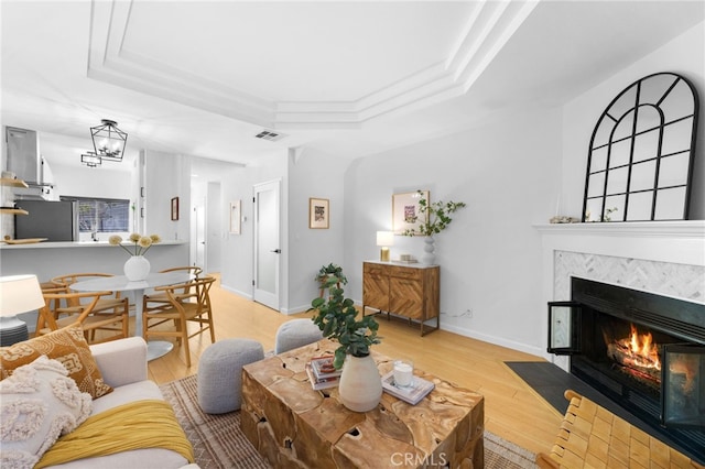 living room with a tray ceiling, ornamental molding, and light wood-type flooring