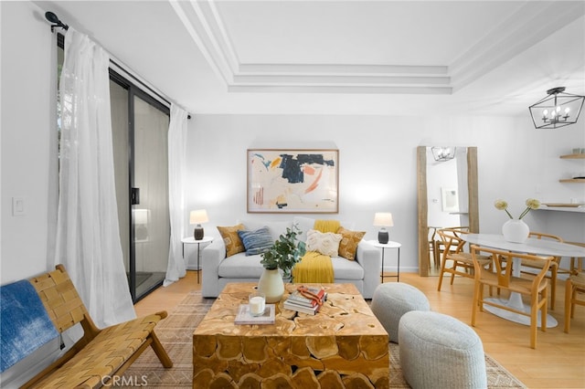 living room featuring crown molding, a raised ceiling, light wood-type flooring, and a notable chandelier