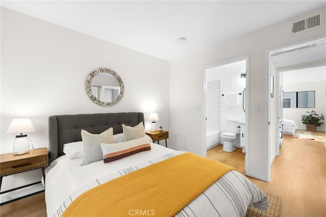 bedroom with ensuite bath and light hardwood / wood-style floors