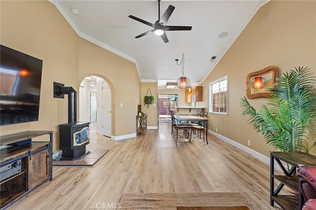 dining room with lofted ceiling, crown molding, a wood stove, light wood-type flooring, and ceiling fan