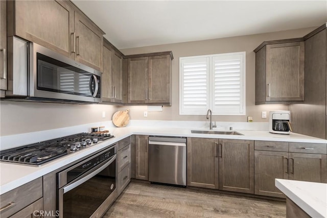 kitchen with light countertops, appliances with stainless steel finishes, a sink, and light wood-style floors