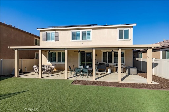 back of property with a patio, a lawn, ceiling fan, and solar panels