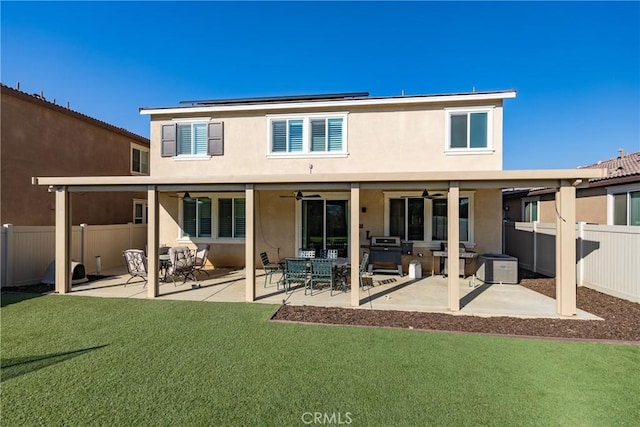 back of property featuring solar panels, fence, a ceiling fan, a yard, and stucco siding