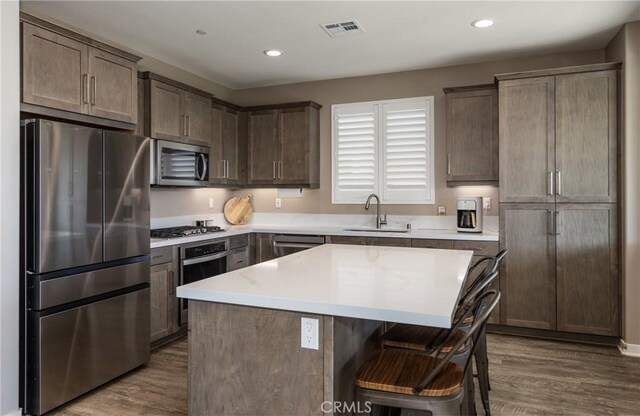 kitchen with sink, a breakfast bar area, appliances with stainless steel finishes, a center island, and dark hardwood / wood-style flooring