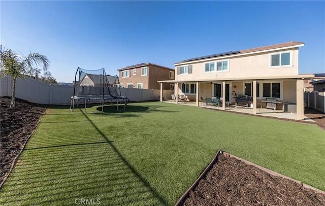 rear view of property featuring a trampoline, a yard, and a patio