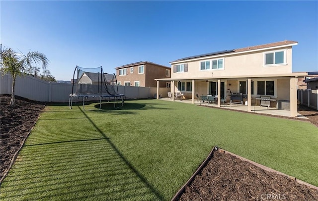 rear view of property featuring a fenced backyard, solar panels, stucco siding, a trampoline, and a patio area