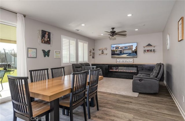 dining area featuring recessed lighting, a ceiling fan, a glass covered fireplace, wood finished floors, and baseboards