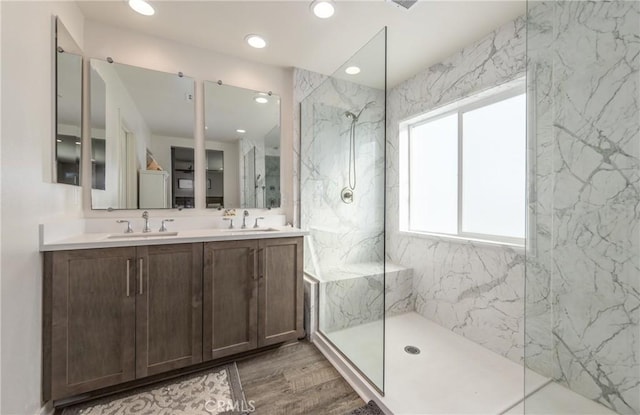 full bath with double vanity, wood finished floors, a sink, and a marble finish shower