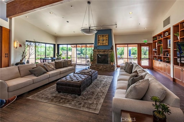 living room featuring dark hardwood / wood-style floors, a stone fireplace, built in shelves, and a high ceiling