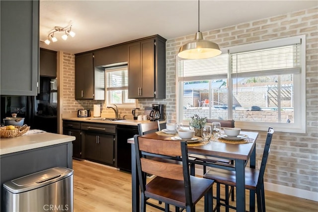 kitchen with brick wall, hanging light fixtures, sink, and light hardwood / wood-style flooring